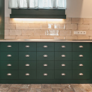 Выдающиеся фото от архитекторов и дизайнеров интерьера: маленькая п-образная кухня-гостиная в стиле кантри с одинарной раковиной, зелеными фасадами, столешницей из ламината, бежевым фартуком, фартуком из сланца, черной техникой, полом из сланца и бежевым полом без острова