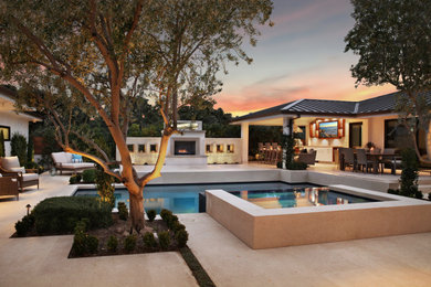 This is an example of a large contemporary courtyard rectangular infinity pool in Orange County with a hot tub and natural stone pavers.