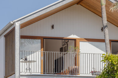 Immagine della villa piccola bianca eclettica a due piani con rivestimento con lastre in cemento, tetto a capanna, copertura in metallo o lamiera, tetto bianco e pannelli e listelle di legno