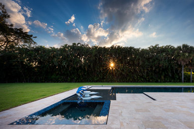 Inspiration for a large modern backyard l-shaped lap pool in Miami with a hot tub and natural stone pavers.