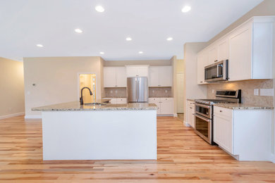 Photo of a mid-sized traditional single-wall kitchen in DC Metro with a double-bowl sink, shaker cabinets, white cabinets, granite benchtops, beige splashback, stone slab splashback, stainless steel appliances, light hardwood floors, with island, brown floor and beige benchtop.