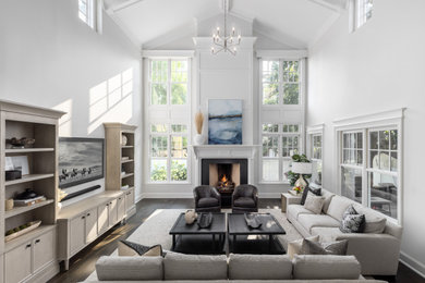 Example of a large classic open concept medium tone wood floor, brown floor, vaulted ceiling and wainscoting living room design in Detroit with gray walls, a standard fireplace, a wood fireplace surround and a wall-mounted tv