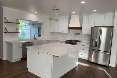 Example of a trendy l-shaped dark wood floor and brown floor kitchen design in Phoenix with a farmhouse sink, shaker cabinets, white cabinets, quartzite countertops, white backsplash, mosaic tile backsplash, stainless steel appliances, an island and white countertops