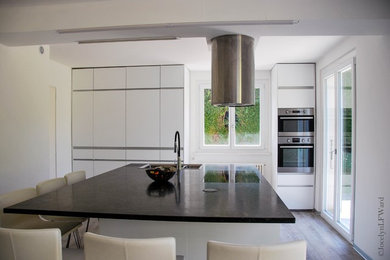 Photo of a medium sized contemporary single-wall open plan kitchen in Other with a double-bowl sink, flat-panel cabinets, white cabinets, granite worktops, black appliances, laminate floors, an island and grey floors.