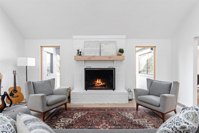 This is an example of a contemporary living room in Indianapolis with white walls, light hardwood floors, a standard fireplace, a brick fireplace surround, brown floor and vaulted.