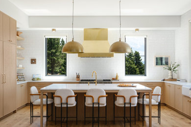 Danish u-shaped medium tone wood floor and brown floor kitchen photo in Other with a farmhouse sink, light wood cabinets, white backsplash, subway tile backsplash, stainless steel appliances, an island and white countertops