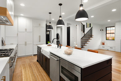 Example of a large trendy l-shaped light wood floor and brown floor eat-in kitchen design in Los Angeles with shaker cabinets, gray cabinets, quartz countertops, an island, white countertops, a farmhouse sink, white backsplash, subway tile backsplash and stainless steel appliances