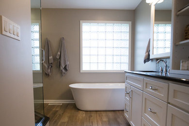 Photo of a mid-sized transitional master bathroom in Chicago with flat-panel cabinets, white cabinets, a freestanding tub, porcelain floors, an undermount sink, granite benchtops, a corner shower, a two-piece toilet, cement tile, beige walls, brown floor, a hinged shower door and beige tile.