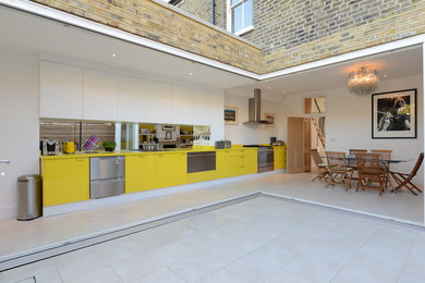 Photo of a mid-sized contemporary galley eat-in kitchen in London with a double-bowl sink, flat-panel cabinets, yellow cabinets, mirror splashback and stainless steel appliances.
