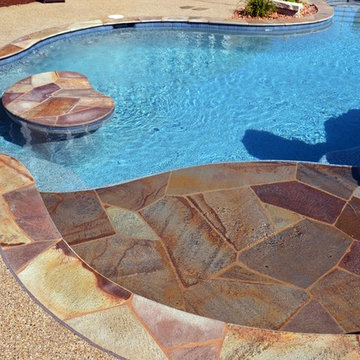 Free form pool with stone table, sun shelf, water feature, and outdoor kitchen,