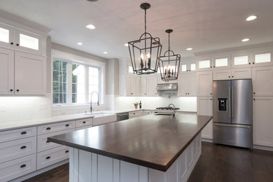 This is an example of a medium sized classic l-shaped kitchen/diner in Boston with a belfast sink, shaker cabinets, white cabinets, engineered stone countertops, white splashback, ceramic splashback, stainless steel appliances, dark hardwood flooring, an island, brown floors and white worktops.