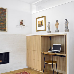Design ideas for a mid-sized modern home office in San Francisco with a built-in desk, white walls, a ribbon fireplace and medium hardwood floors.