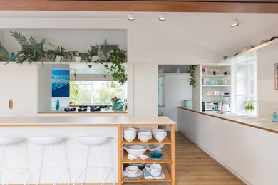 This is an example of a contemporary kitchen in Brisbane with white cabinets, light hardwood floors, a peninsula, beige floor and white benchtop.