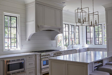 Example of a mid-sized country l-shaped enclosed kitchen design in Chicago with a farmhouse sink, shaker cabinets, white cabinets, white backsplash, wood backsplash, stainless steel appliances, an island and white countertops