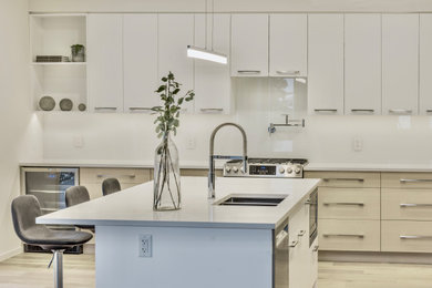 Trendy l-shaped light wood floor and beige floor kitchen photo in Other with an undermount sink, flat-panel cabinets, beige cabinets, quartz countertops, white backsplash, glass sheet backsplash, stainless steel appliances, an island and white countertops