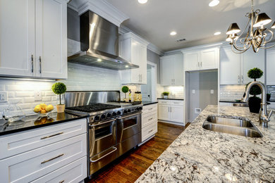 Open concept kitchen - large traditional l-shaped dark wood floor and brown floor open concept kitchen idea in Atlanta with a double-bowl sink, shaker cabinets, white cabinets, granite countertops, white backsplash, subway tile backsplash, stainless steel appliances, an island and black countertops