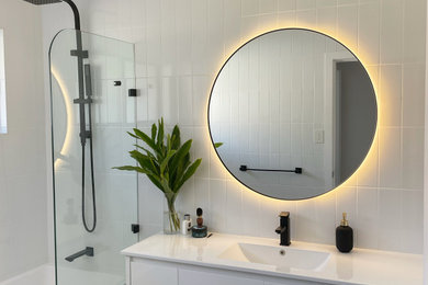 Photo of a modern bathroom in Sydney with white cabinets, a drop-in tub, a shower/bathtub combo, a two-piece toilet, white tile, ceramic tile, white walls, ceramic floors, an integrated sink, engineered quartz benchtops, black floor, an open shower, white benchtops, a single vanity and a freestanding vanity.
