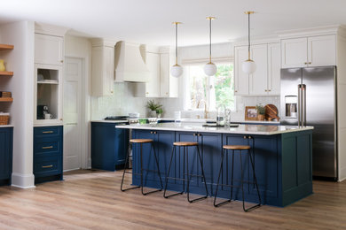 Example of a large transitional l-shaped vinyl floor and brown floor eat-in kitchen design in Charlotte with a farmhouse sink, raised-panel cabinets, blue cabinets, quartzite countertops, white backsplash, ceramic backsplash, stainless steel appliances, an island and beige countertops