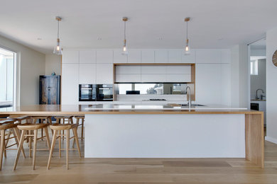 This is an example of a large scandinavian kitchen in Sydney with a double-bowl sink, quartz benchtops, mirror splashback, black appliances and light hardwood floors.
