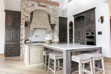 Huge tuscan l-shaped light wood floor open concept kitchen photo in Denver with raised-panel cabinets, dark wood cabinets, quartzite countertops, white backsplash, ceramic backsplash, stainless steel appliances, two islands and gray countertops
