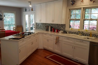 Inspiration for a mid-sized transitional u-shaped kitchen in Atlanta with a drop-in sink, stainless steel appliances, medium hardwood floors, brown floor, multi-coloured splashback, stone tile splashback, white benchtop, shaker cabinets, white cabinets, solid surface benchtops and a peninsula.