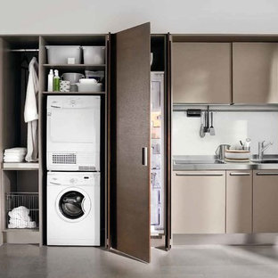 ニューヨークの小さいモダンスタイルのおしゃれな家事室 (ドロップインシンク、フラットパネル扉のキャビネット、ステンレスカウンター、白い壁、コンクリートの床、上下配置の洗濯機・乾燥機、グレーの床、茶色いキャビネット) の写真