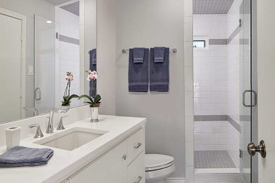 Example of a mid-sized minimalist kids' white tile and subway tile ceramic tile, gray floor and single-sink corner shower design in Dallas with flat-panel cabinets, white cabinets, a two-piece toilet, gray walls, an undermount sink, quartz countertops, a hinged shower door, white countertops and a built-in vanity