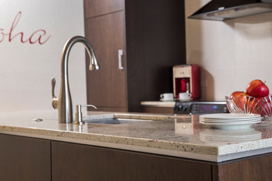 Open concept kitchen - mid-sized contemporary galley porcelain tile open concept kitchen idea in Hawaii with a single-bowl sink, flat-panel cabinets, dark wood cabinets, granite countertops, white backsplash, ceramic backsplash, black appliances and an island
