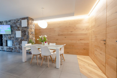 Immagine di un'ampia sala da pranzo aperta verso il soggiorno design con pareti marroni, pavimento in legno massello medio, camino lineare Ribbon, cornice del camino in pietra, pavimento beige, soffitto ribassato e pareti in legno