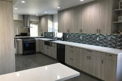 This is an example of a large contemporary u-shaped open plan kitchen in San Diego with a farmhouse sink, flat-panel cabinets, light wood cabinets, quartz benchtops, grey splashback, glass tile splashback, stainless steel appliances, a peninsula, grey floor, white benchtop and porcelain floors.