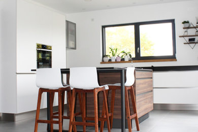Cette image montre une grande cuisine ouverte minimaliste en L avec des portes de placard blanches, îlot et un sol gris.