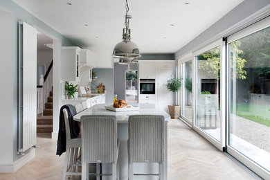 This is an example of a mid-sized transitional l-shaped eat-in kitchen in Dublin with recessed-panel cabinets, white cabinets, quartzite benchtops, white splashback, light hardwood floors, with island, beige floor and subway tile splashback.