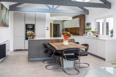 Photo of a mid-sized contemporary l-shaped eat-in kitchen in Berkshire with an undermount sink, flat-panel cabinets, white cabinets, black appliances, with island, grey floor and white benchtop.