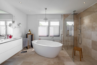 Photo of a large contemporary ensuite bathroom in Dusseldorf with flat-panel cabinets, white cabinets, a freestanding bath, a built-in shower, beige tiles, travertine tiles, white walls, travertine flooring, an integrated sink, beige floors, an open shower, white worktops, a single sink and a floating vanity unit.