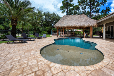 Photo of a large beach style backyard custom-shaped natural pool in Miami with a hot tub and decking.