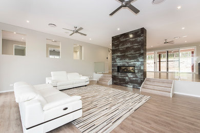Photo of a large modern formal open concept living room in Sunshine Coast with beige walls, laminate floors, a two-sided fireplace, a tile fireplace surround, a wall-mounted tv and brown floor.
