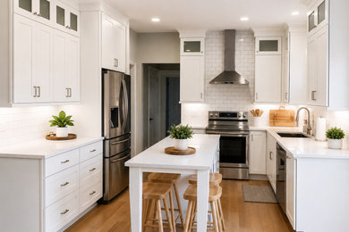 Large trendy u-shaped light wood floor eat-in kitchen photo in Other with an undermount sink, shaker cabinets, white cabinets, quartz countertops, white backsplash, ceramic backsplash, stainless steel appliances, an island and white countertops
