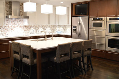 Bild på ett funkis kök, med en dubbel diskho, rostfria vitvaror, brunt stänkskydd, bänkskiva i kvarts, släta luckor och en köksö