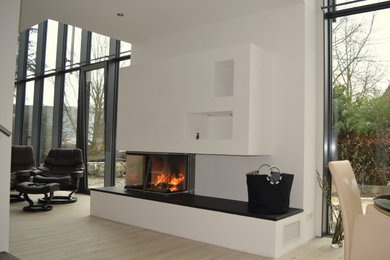 Großes Modernes Wohnzimmer im Loft-Stil mit weißer Wandfarbe, hellem Holzboden, Kamin, verputzter Kaminumrandung und beigem Boden in Sonstige