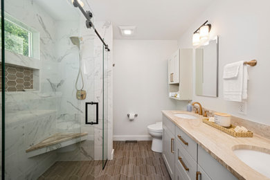 Inspiration for a small transitional master bathroom in Seattle with recessed-panel cabinets, beige cabinets, a curbless shower, a bidet, white tile, stone tile, white walls, porcelain floors, an undermount sink, marble benchtops, brown floor, a sliding shower screen, beige benchtops, a shower seat, a double vanity and a built-in vanity.