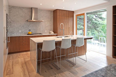 Example of a mid-sized minimalist single-wall light wood floor and beige floor open concept kitchen design in Calgary with an undermount sink, flat-panel cabinets, beige cabinets, marble countertops, gray backsplash, marble backsplash, paneled appliances and an island