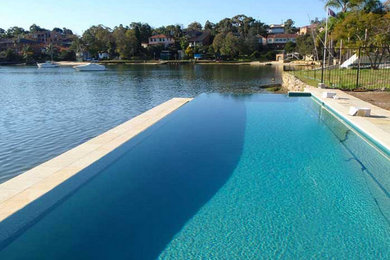 Design ideas for a large modern backyard rectangular infinity pool in Sydney with natural stone pavers.