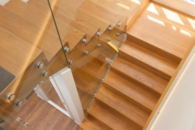 Ejemplo de escalera en U actual de tamaño medio con escalones de madera, contrahuellas de madera y barandilla de vidrio