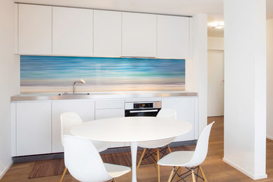 Design ideas for a small beach style separate kitchen in Sunshine Coast with an integrated sink, stainless steel benchtops, blue splashback, glass sheet splashback, stainless steel appliances, medium hardwood floors and brown floor.