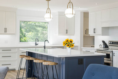 Inspiration for a large transitional l-shaped medium tone wood floor and brown floor open concept kitchen remodel in Toronto with an undermount sink, recessed-panel cabinets, white cabinets, solid surface countertops, stainless steel appliances, an island and white countertops