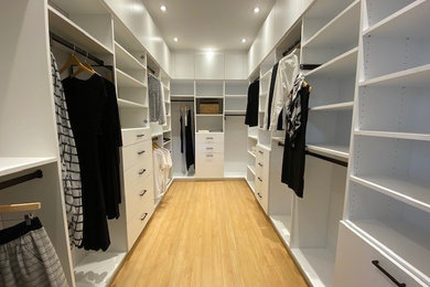 Inspiration for a large modern gender-neutral medium tone wood floor walk-in closet remodel in Montreal with open cabinets and white cabinets