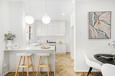 Photo of a small modern u-shaped kitchen in Sydney with a drop-in sink, quartz benchtops, white splashback, ceramic splashback, black appliances, medium hardwood floors and beige benchtop.
