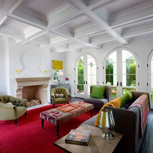 Modelo de salón abierto, mediterráneo, con paredes blancas, suelo de madera oscura, chimenea tradicional y marco de chimenea de hormigón