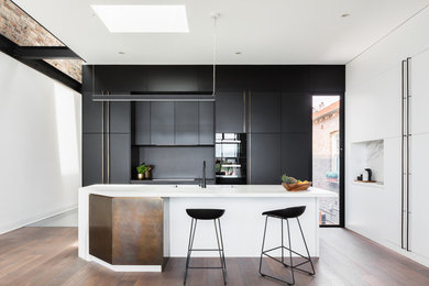 This is an example of a contemporary l-shaped kitchen in Sydney with medium hardwood floors, brown floor, an integrated sink, flat-panel cabinets, black splashback, panelled appliances, with island and white benchtop.