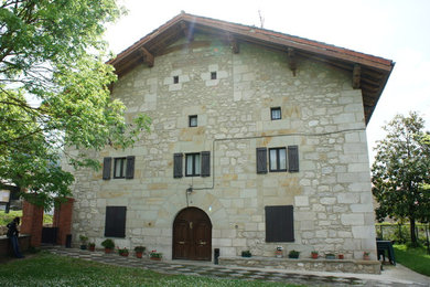 This is an example of a large country three-storey grey exterior in Bilbao with stone veneer and a gable roof.